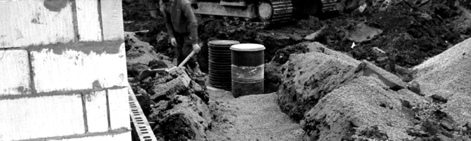 Operative digging around drainage chambers in an open trench next to a block wall