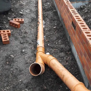 Orange drainage pipe and junction laid in a trench beside a new brick wall