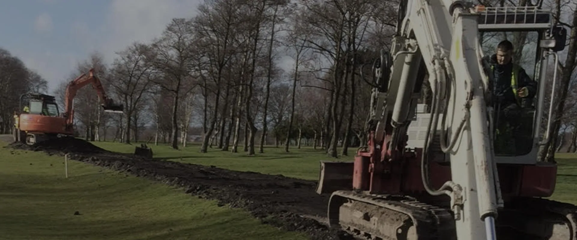 OGC excavator digging a trench across open parkland