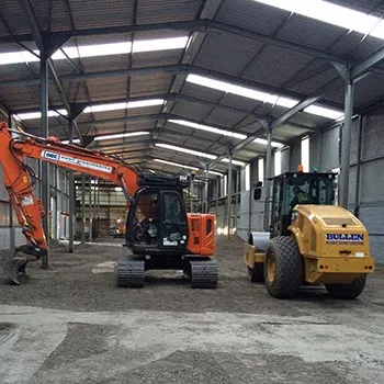 Excavator and roller working on a prepared sub-base inside an industrial building