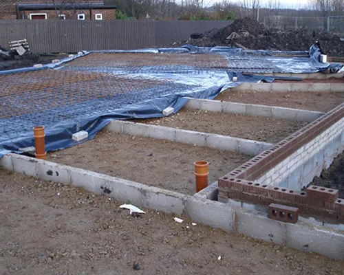 Substructure with blue membrane laid and orange drainage pipes coming through the slab area